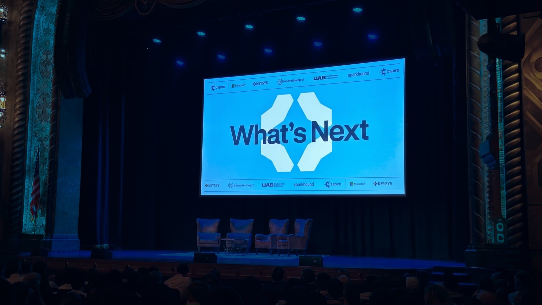 The Alabama Theatre stage on June 23, What's Next on the screen above the panel chairs, the crowd in the foreground